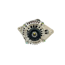 An automotive alternator with a silver aluminum housing and black center hub, resting on a white surface with a blurred auto parts warehouse background.