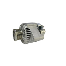 A silver metallic automotive alternator resting on a white surface with a blurred workshop or garage background.