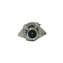 A silver metallic automotive alternator resting on a white surface with a blurred warehouse background.
