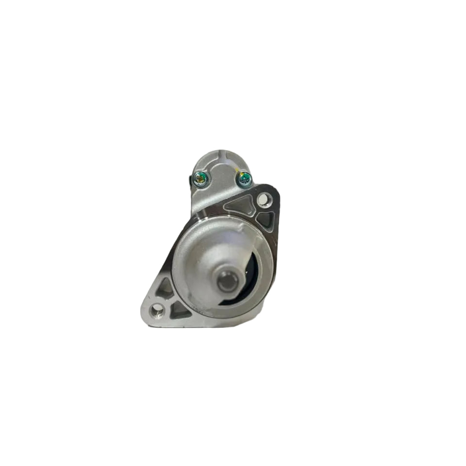 A silver metal automotive starter motor with a mounting bracket, photographed on a white surface with a blurred warehouse background.