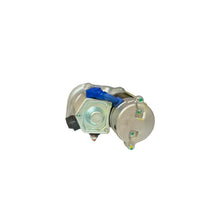 A small metallic mechanical component with a blue plastic piece on top, resting on a white surface inside a blurred retail or workshop environment with shelves in the background.