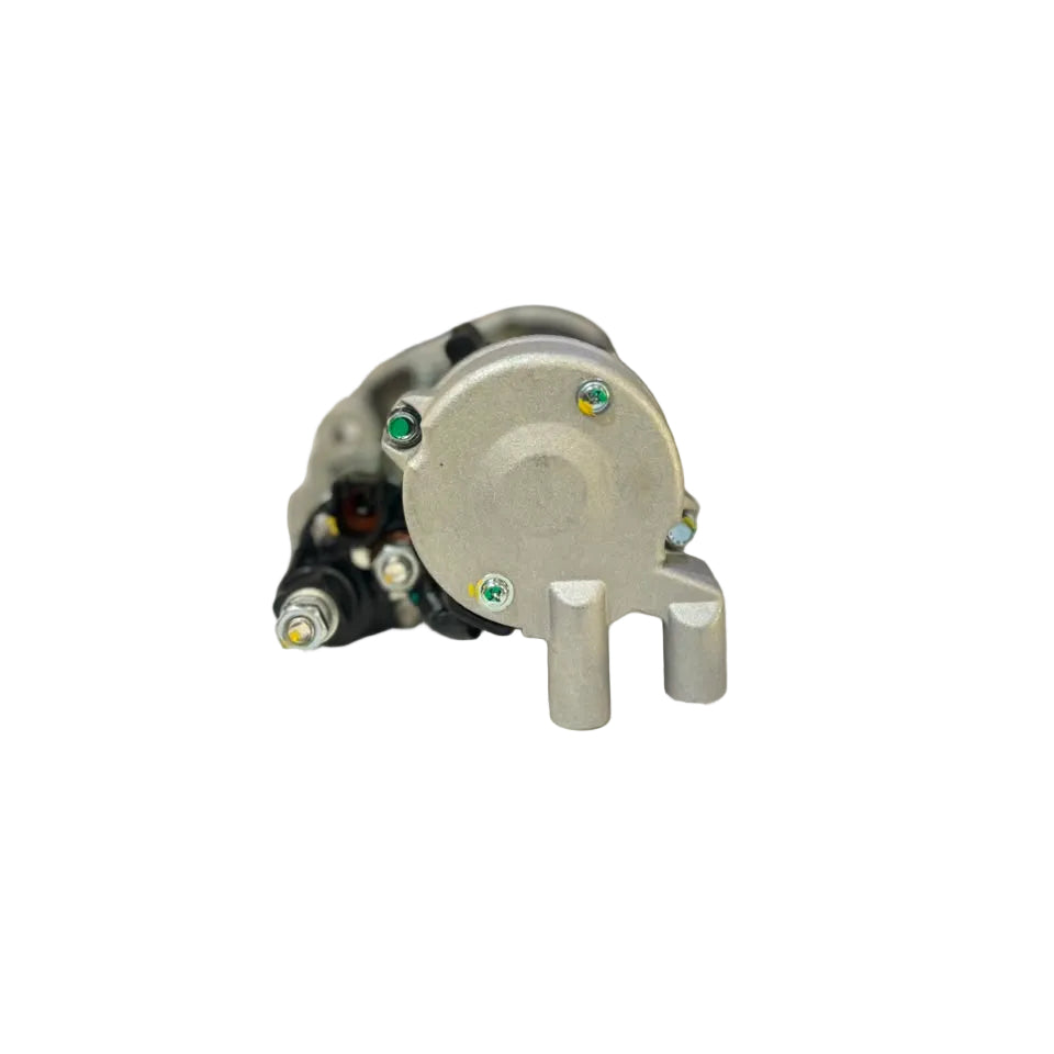 A used silver metal automotive alternator resting on a white surface, with a blurred auto parts store background.